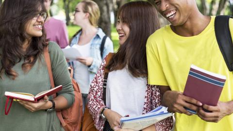 Three diverse students walking together holding books.