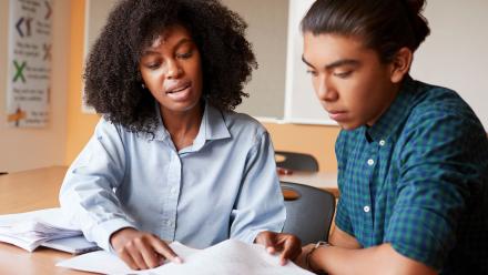 Black high school female teacher helping Latino teen with reading