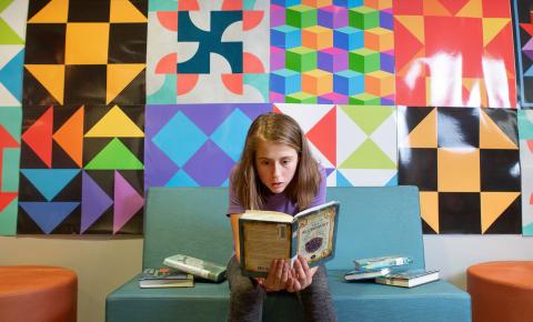 Middle school girl reading in front of colorful wall